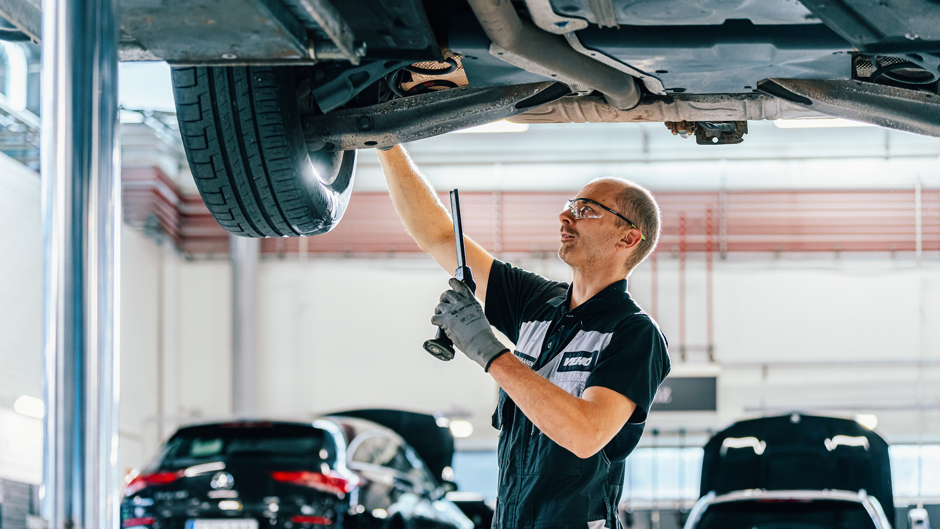 Mercedes mehāniķis zem automašīnas pārbauda atbalsta sviru klīrensus.