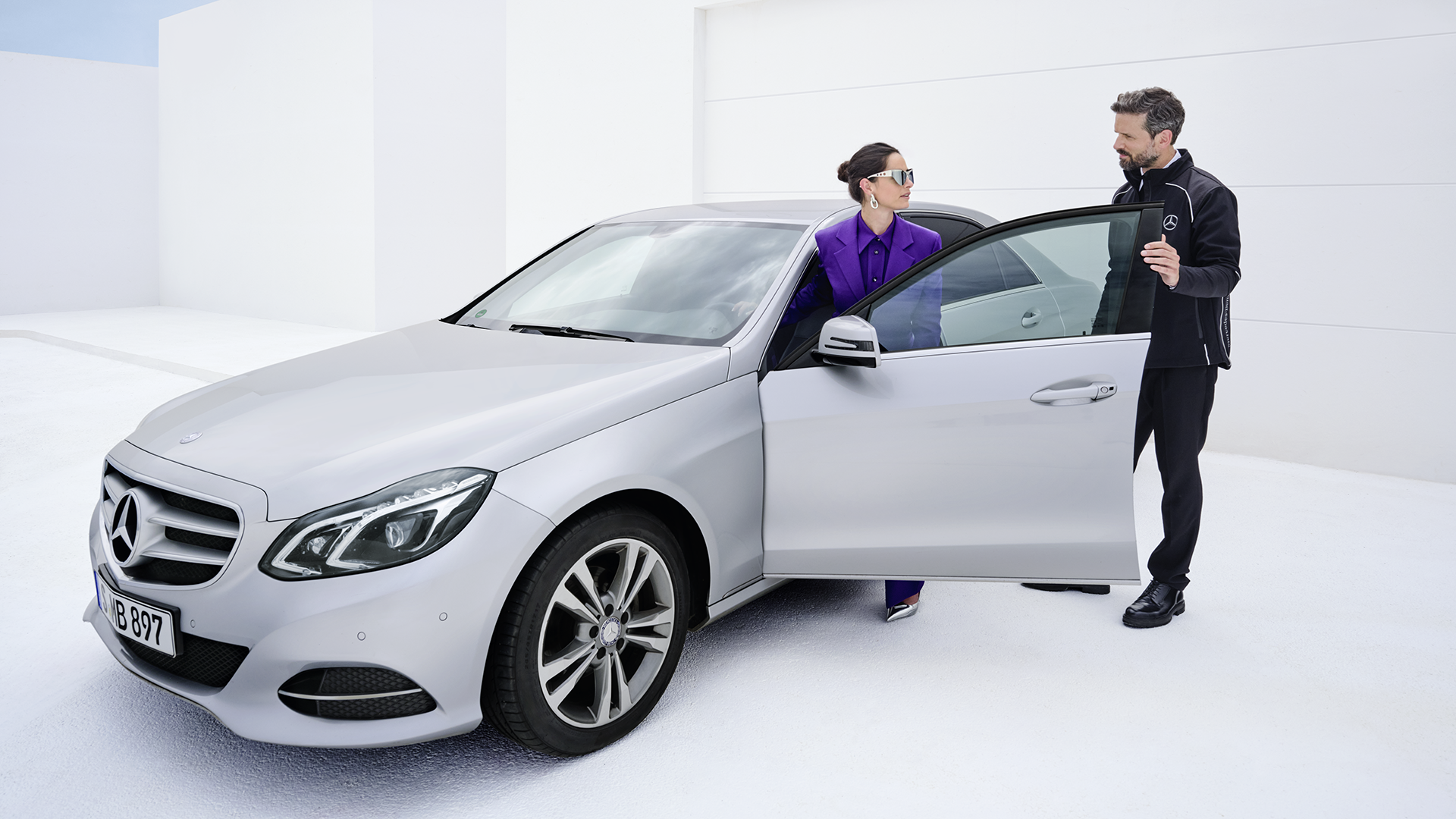 Klients un klientu apkalpošanas pārstāvis blakus sudrabpelēkam Mercedes-Benz E-klases auto