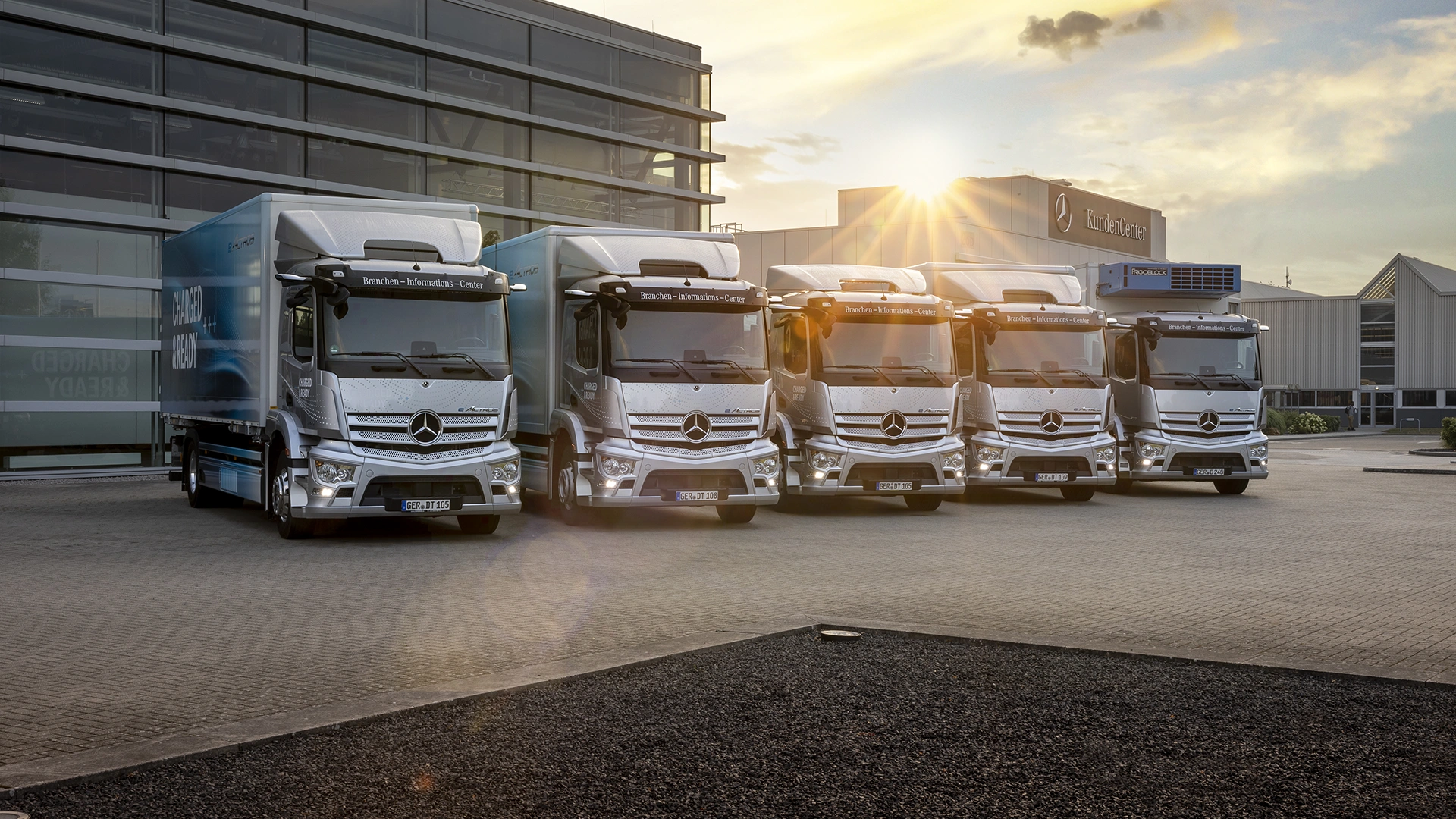 Piecas pilnībā elektriskās Mercedes-Benz kravas automašīnas, kas izkārtotas ēkas priekšā