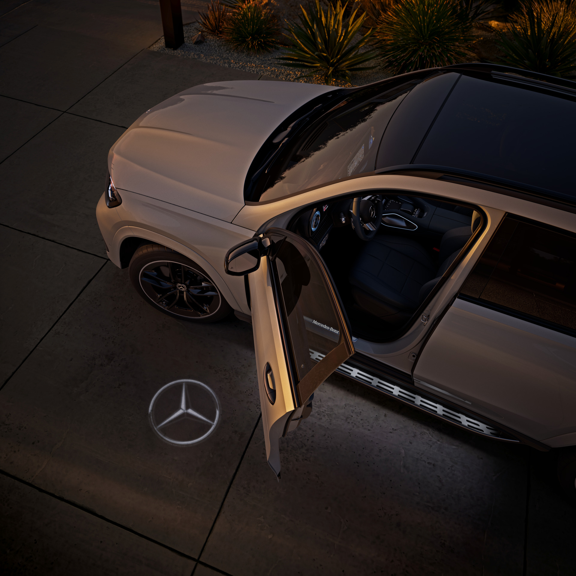 Balts Mercedes-Benz GLE ar atvērtām vadītāja durvīm un zvaigznes gaismas projekciju uz zemes